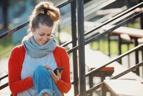 A person sitting outside on their cellphone looking up information about ovulation and the fertility window.