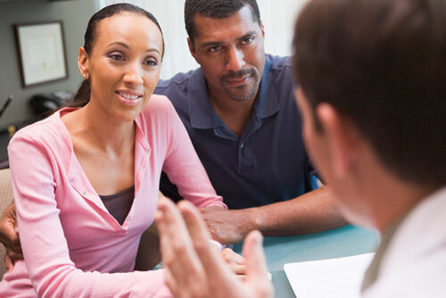 Two people sit at a table facing a doctor