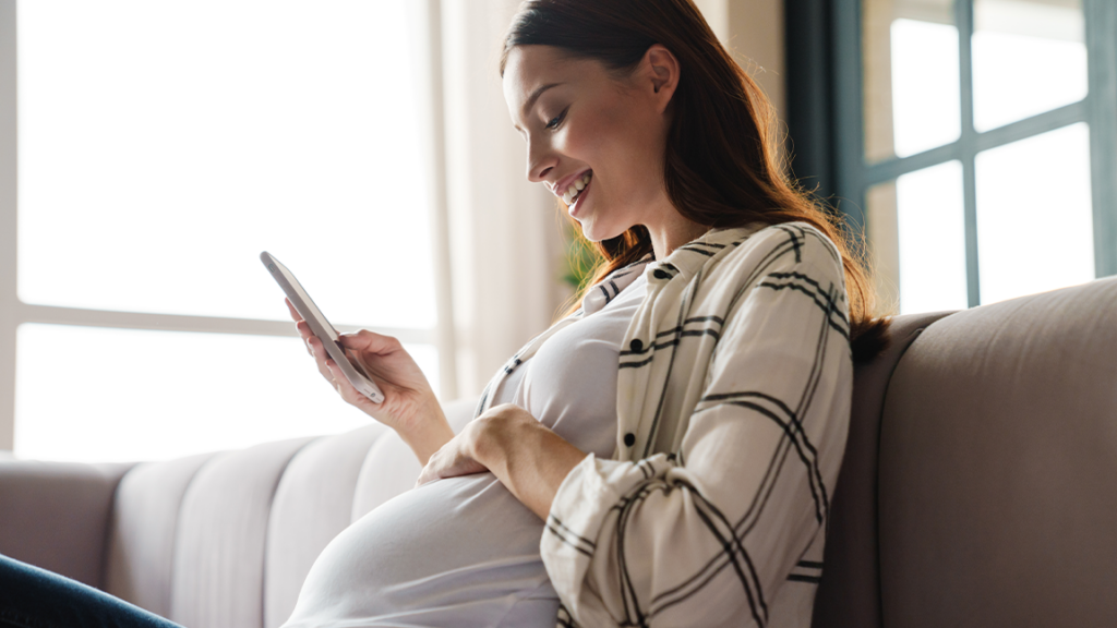 Pregnant woman smiling while looking at phone